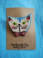 Porcelain brooch of a cat wearing a pink polkadot bow tie