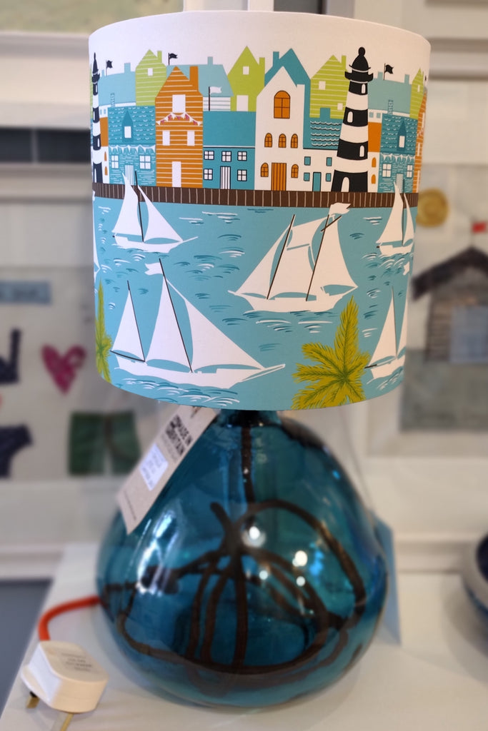 Coastal harbour lampshade shown on a blue recycled glass lamp-base